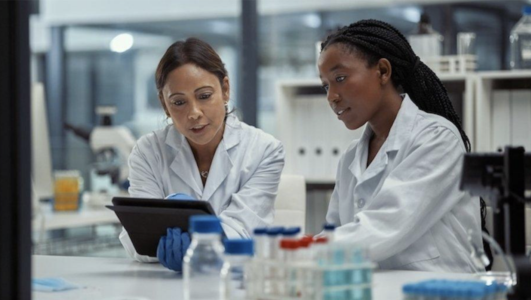 Two scientists in lab coats examining research data on tablet